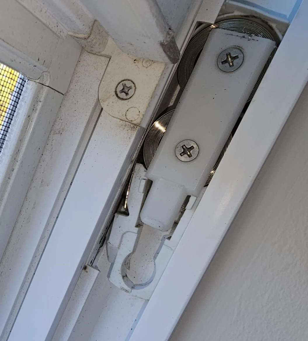 Close-up of window balance hardware in the side track beside a white sash.