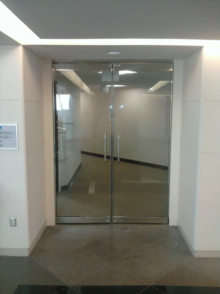 Clear double glass doors with metal pull handles in a finished corridor.