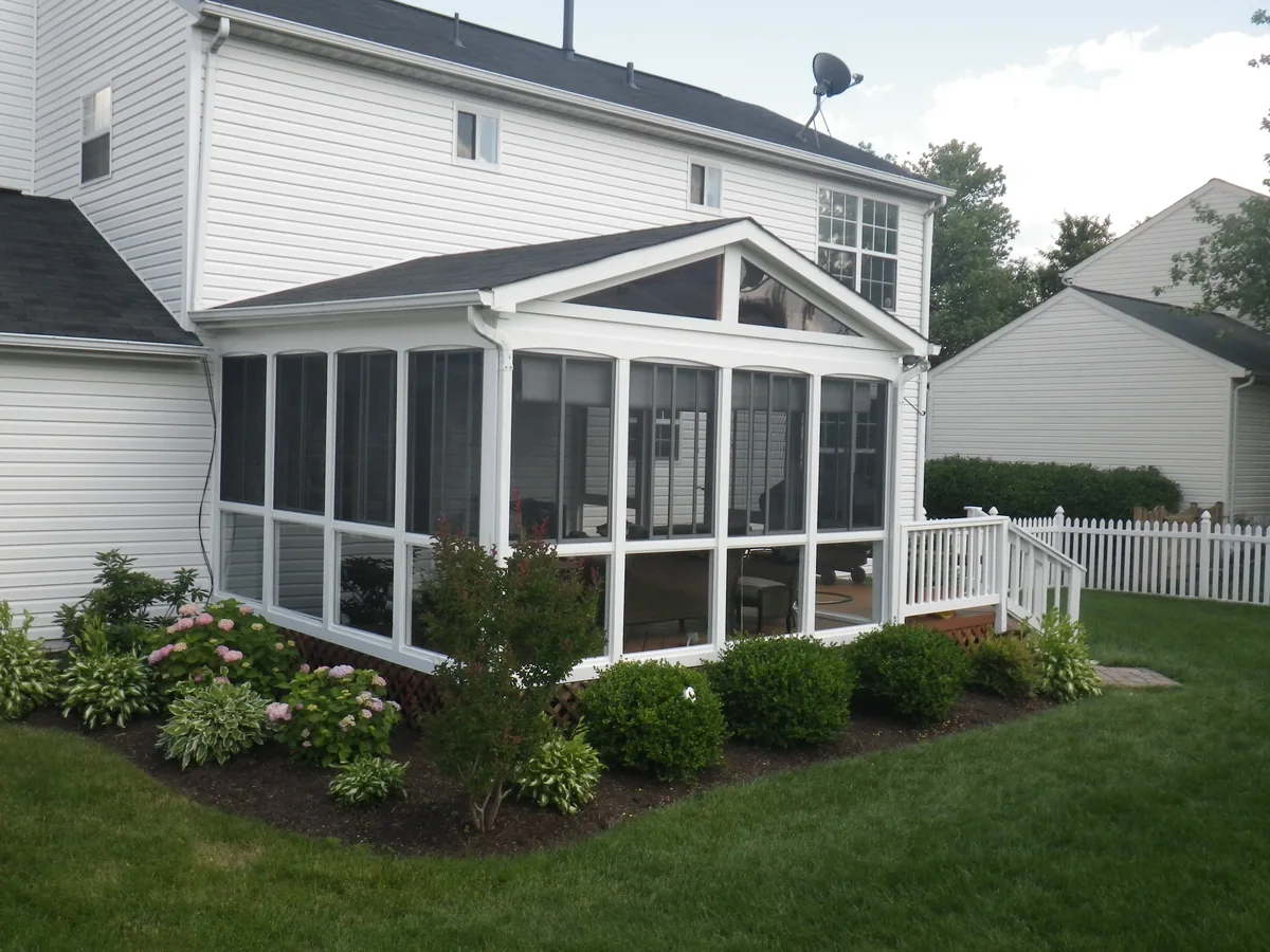 White-framed gabled screened porch beside a landscaped lawn.