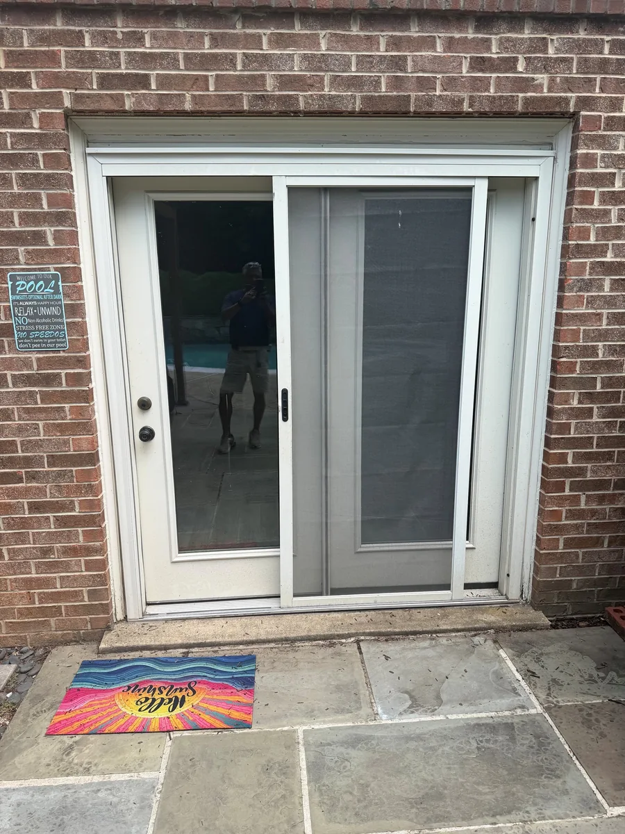 White sliding patio screen door beside a glass door in a brick wall.