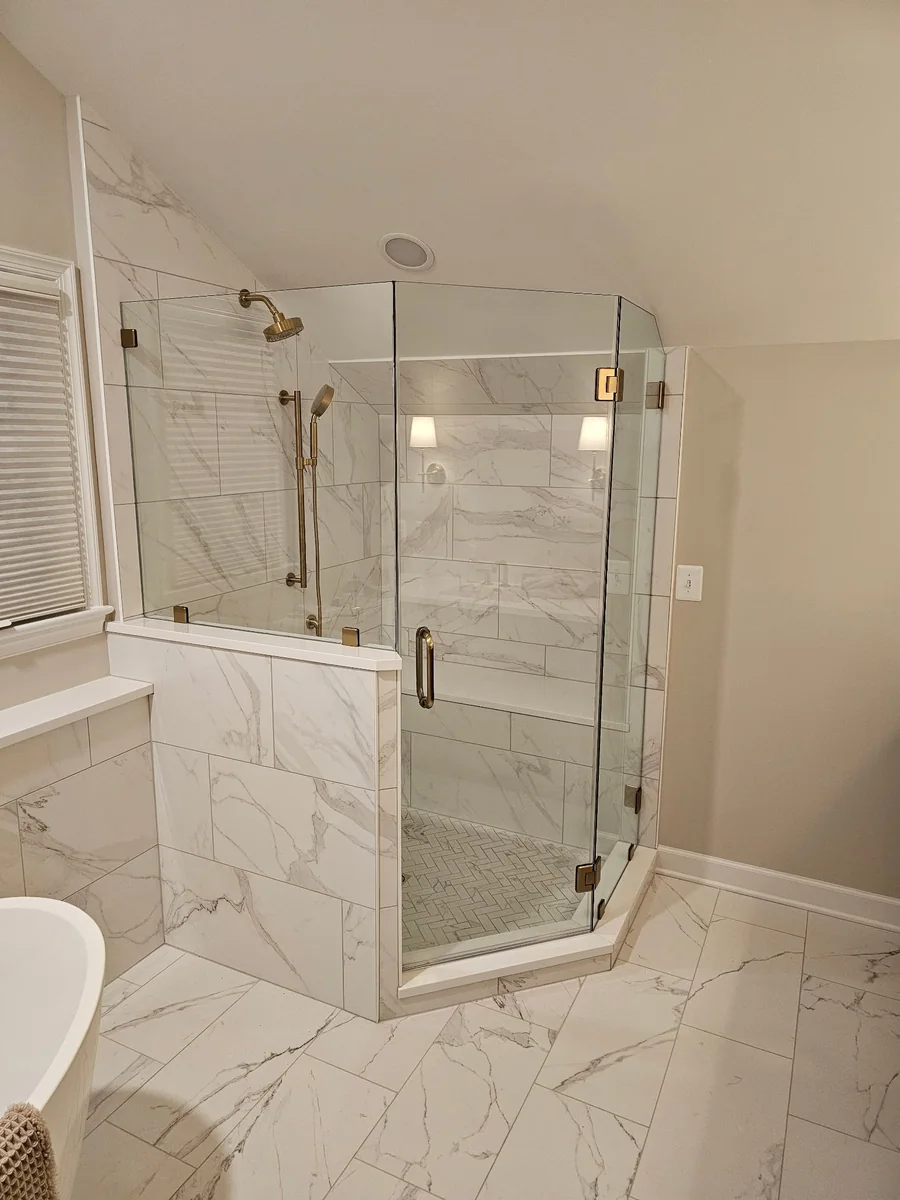 Frameless glass shower enclosure with gold-tone hardware beside a bathtub.