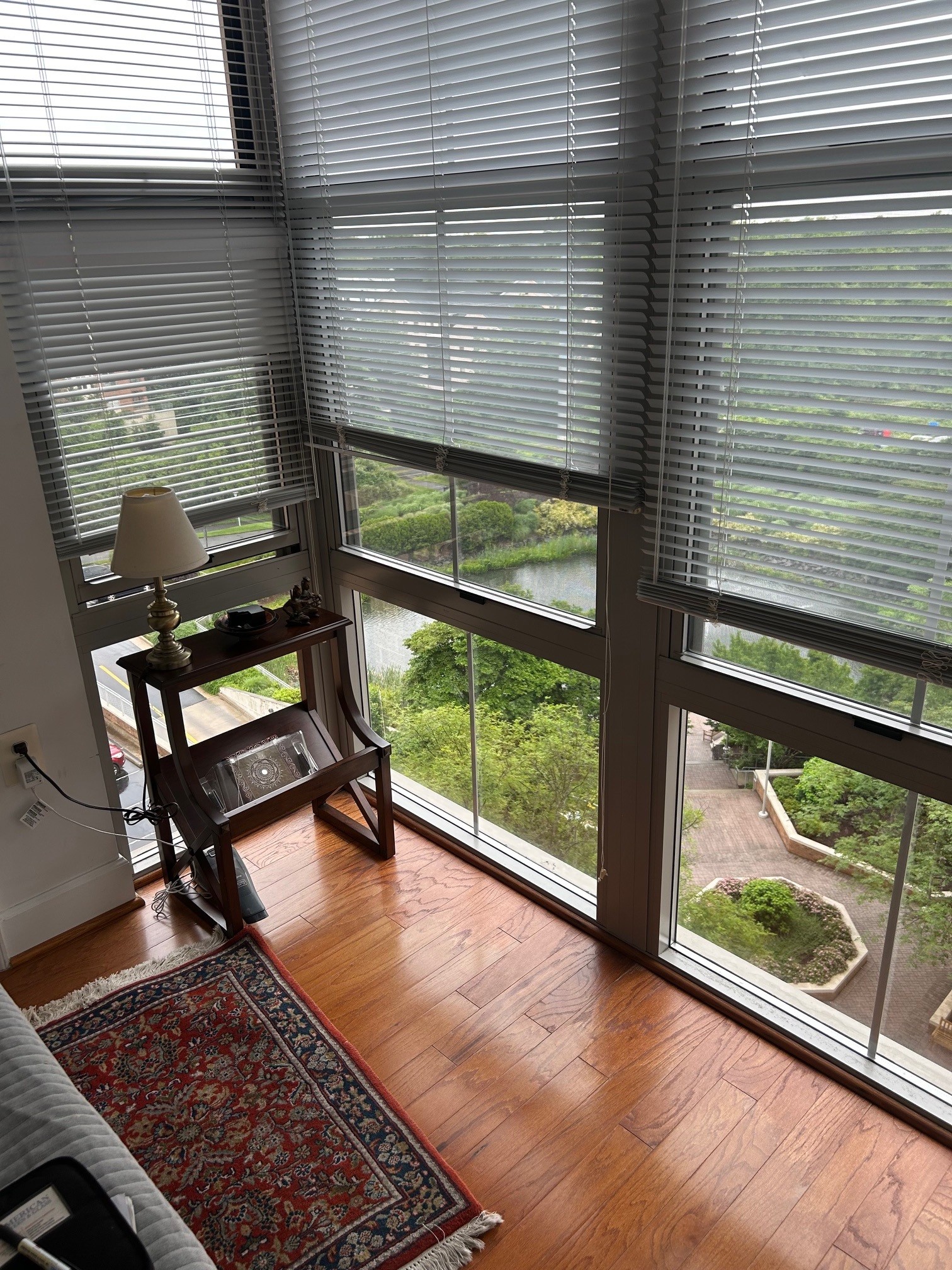 Floor-to-ceiling corner windows with blinds overlooking a landscaped courtyard and water