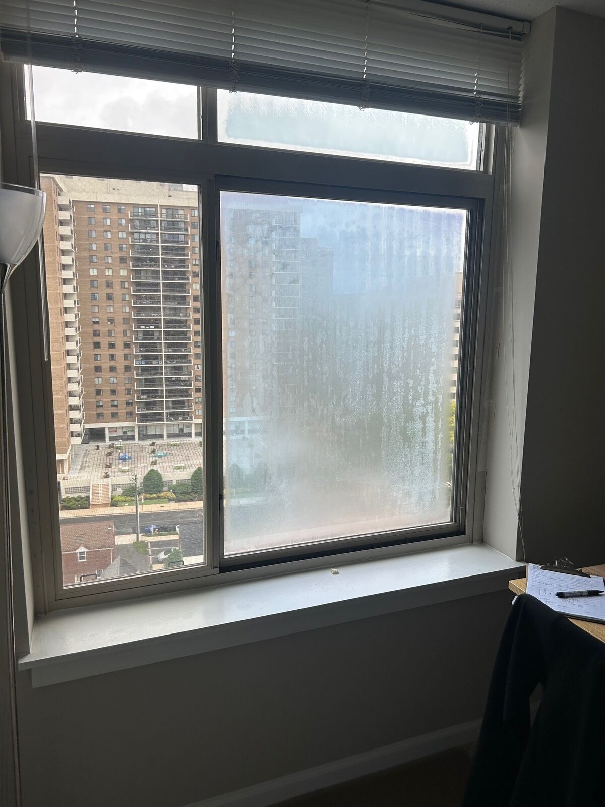 An apartment window with a fogged lower pane looking out on nearby high-rise buildings