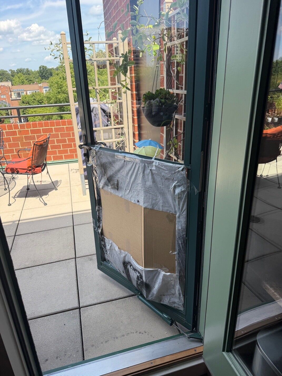 An open green-framed commercial glass door with a damaged panel taped during work