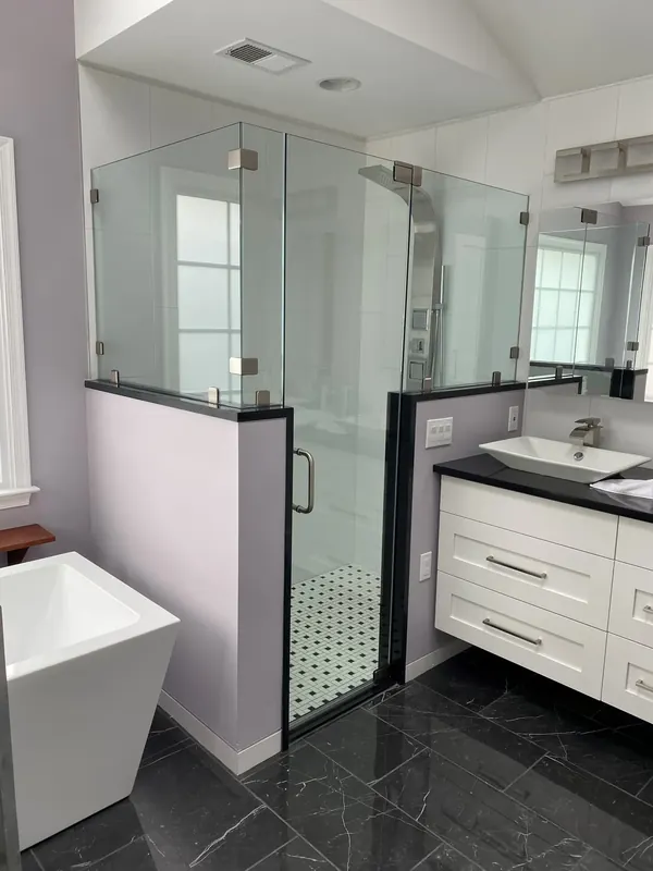 Glass shower between a white vanity and freestanding tub.