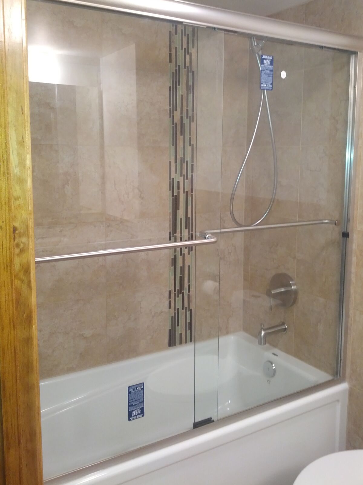 Sliding glass doors over a bathtub with beige tile, a vertical mosaic accent strip and a towel bar on the glass