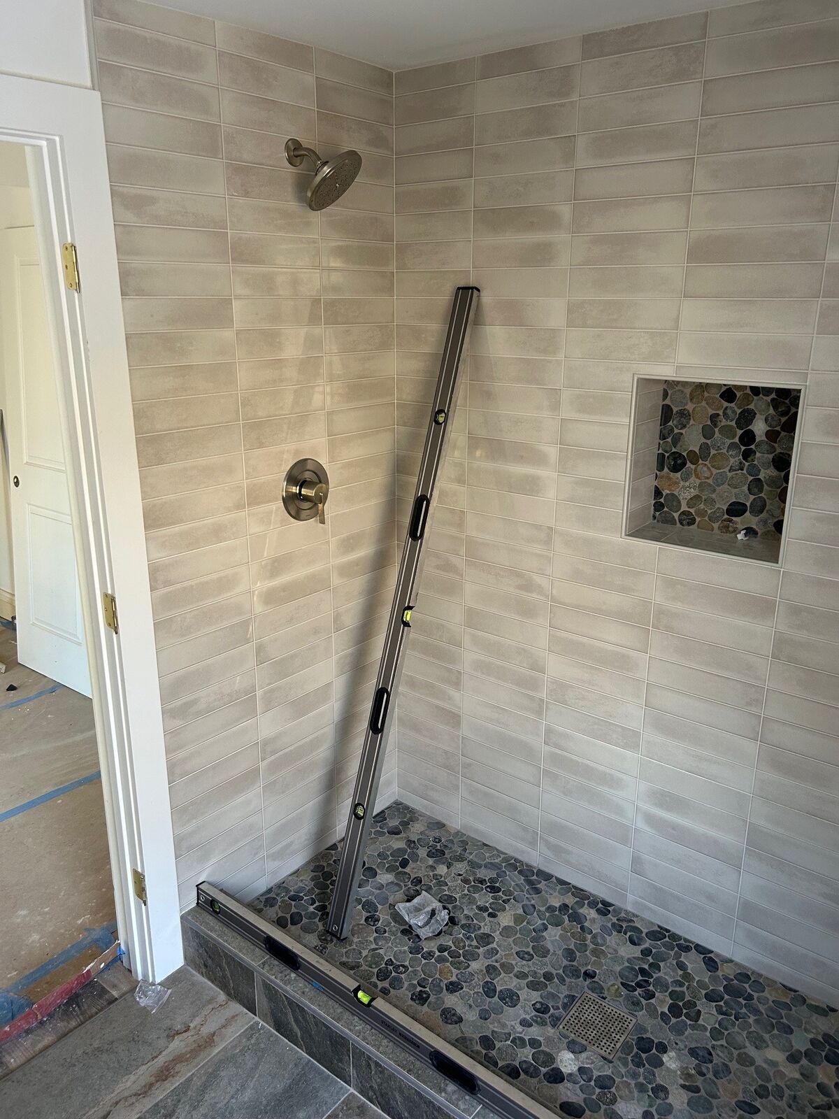 A finished tiled shower opening with a level leaning inside, before the glass is measured