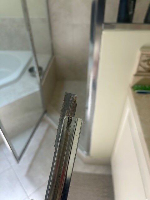 A close-up of a metal channel at the edge of a shower glass panel