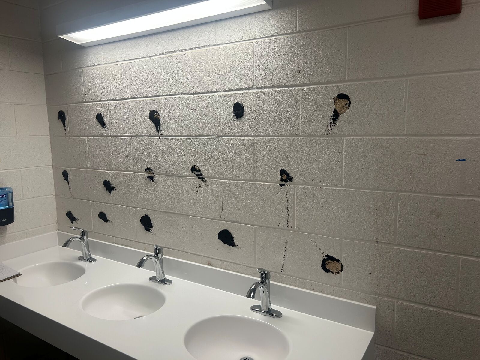 Adhesive marks on a wall above a three-sink restroom counter after a mirror was removed