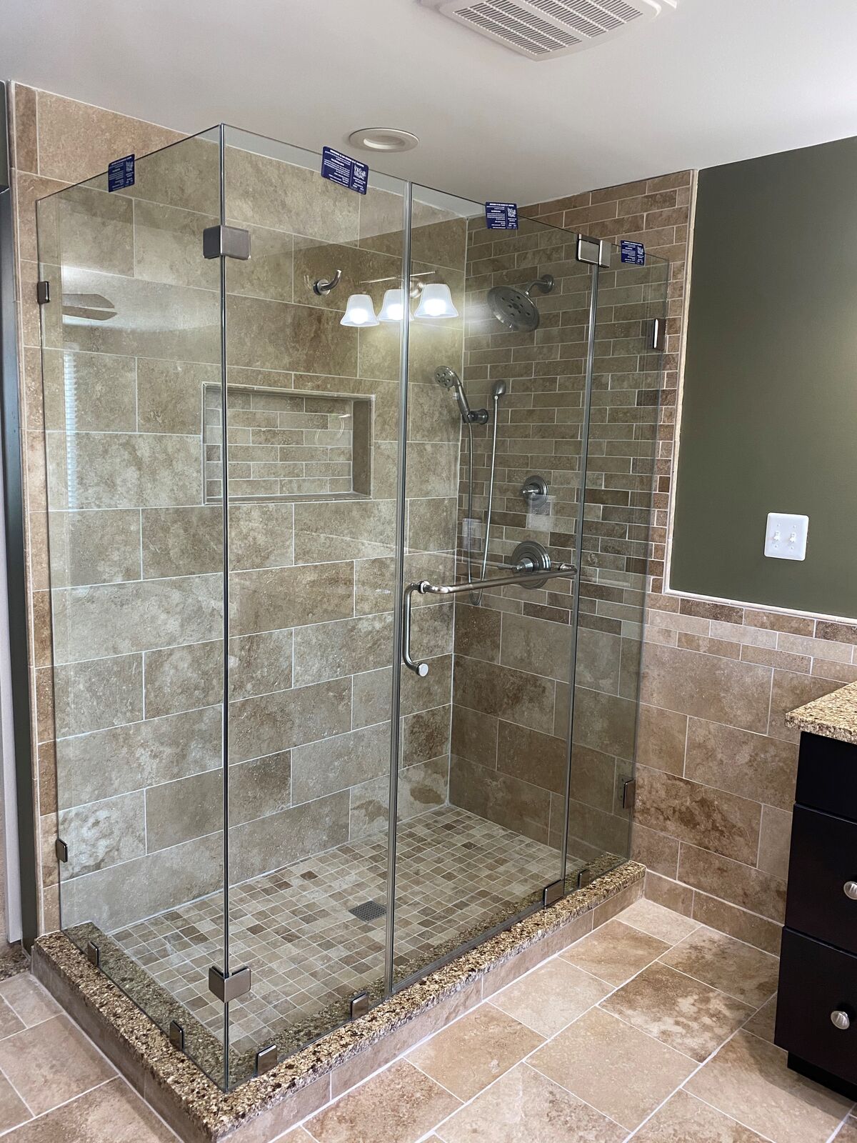 A frameless corner shower with warm stone-look tile and chrome hinges