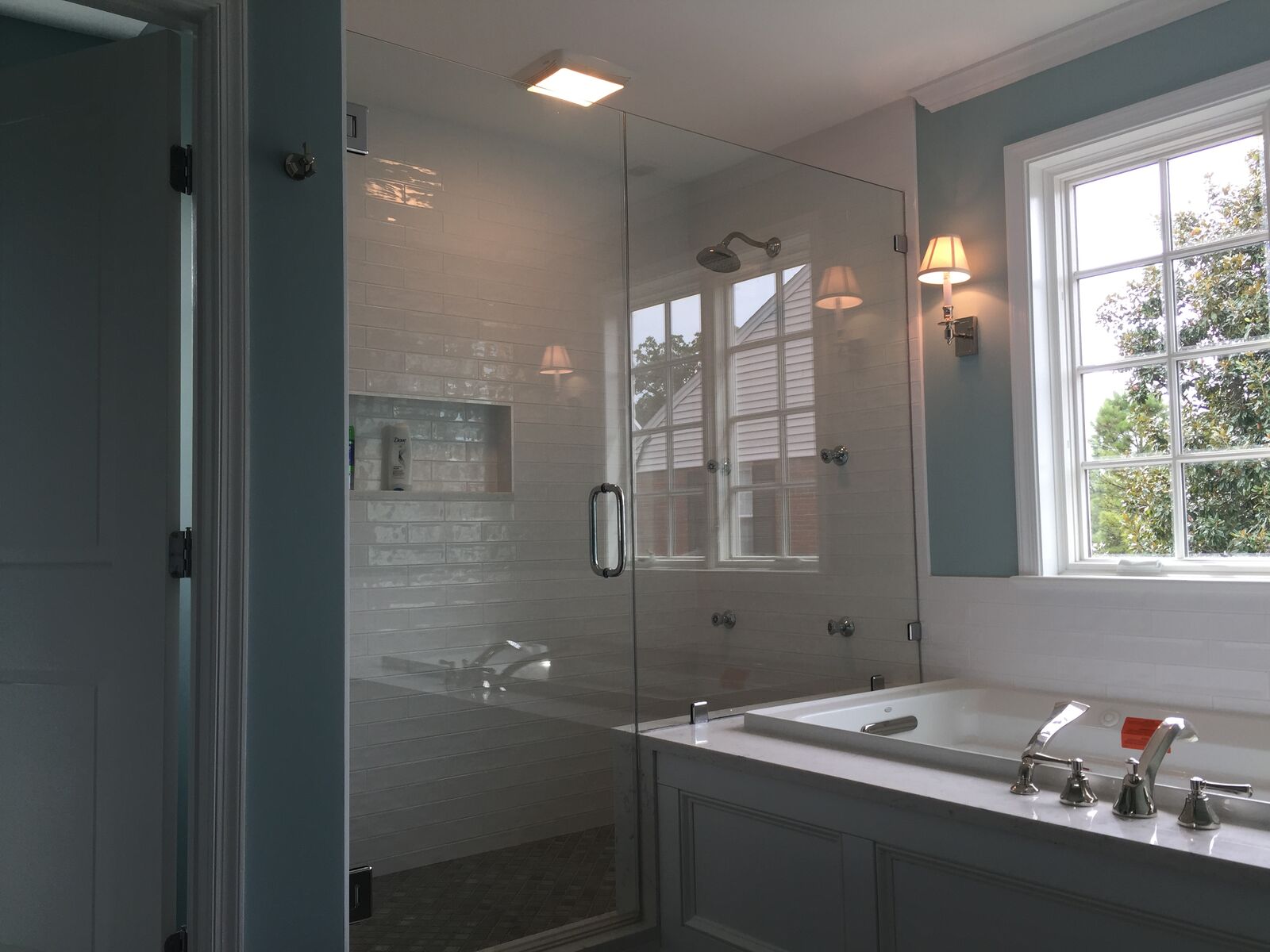 A frameless glass shower beside a built-in bathtub under a window