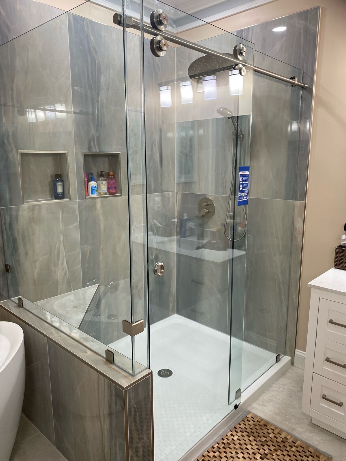 A wide view of a frameless sliding shower with gray tile and a fixed panel beside a freestanding tub